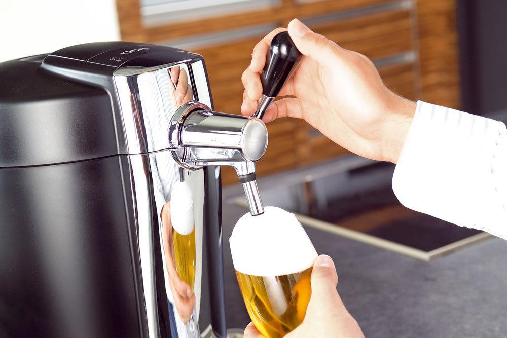 Das Bild zeigt eine Hand, die den Hebel der Zapfmaschine bedient, während eine andere Hand das Glas unter den Hahn hält. Der Hintergrund ist unscharf.