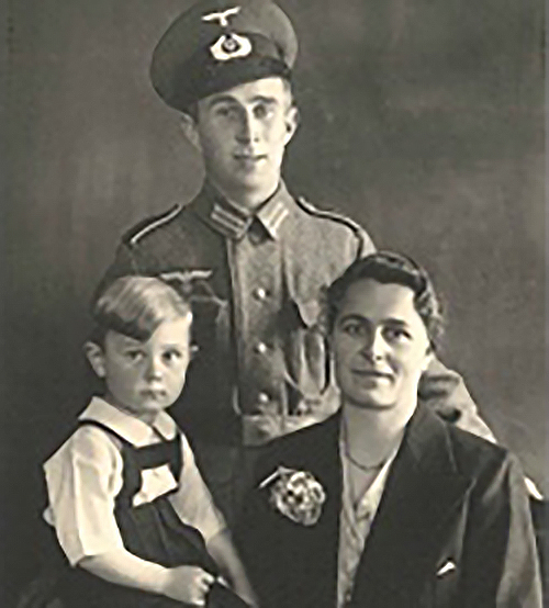 Ein historisches Foto von Alfred Linzgieseder Senior mit seinem Sohn Arnold und seiner Frau Agnes, bevor er in den Krieg zog. Alfred trägt eine Uniform, während Agnes und Arnold in der typischen Kleidung der Zeit zu sehen sind. Die Szene fängt einen Momen