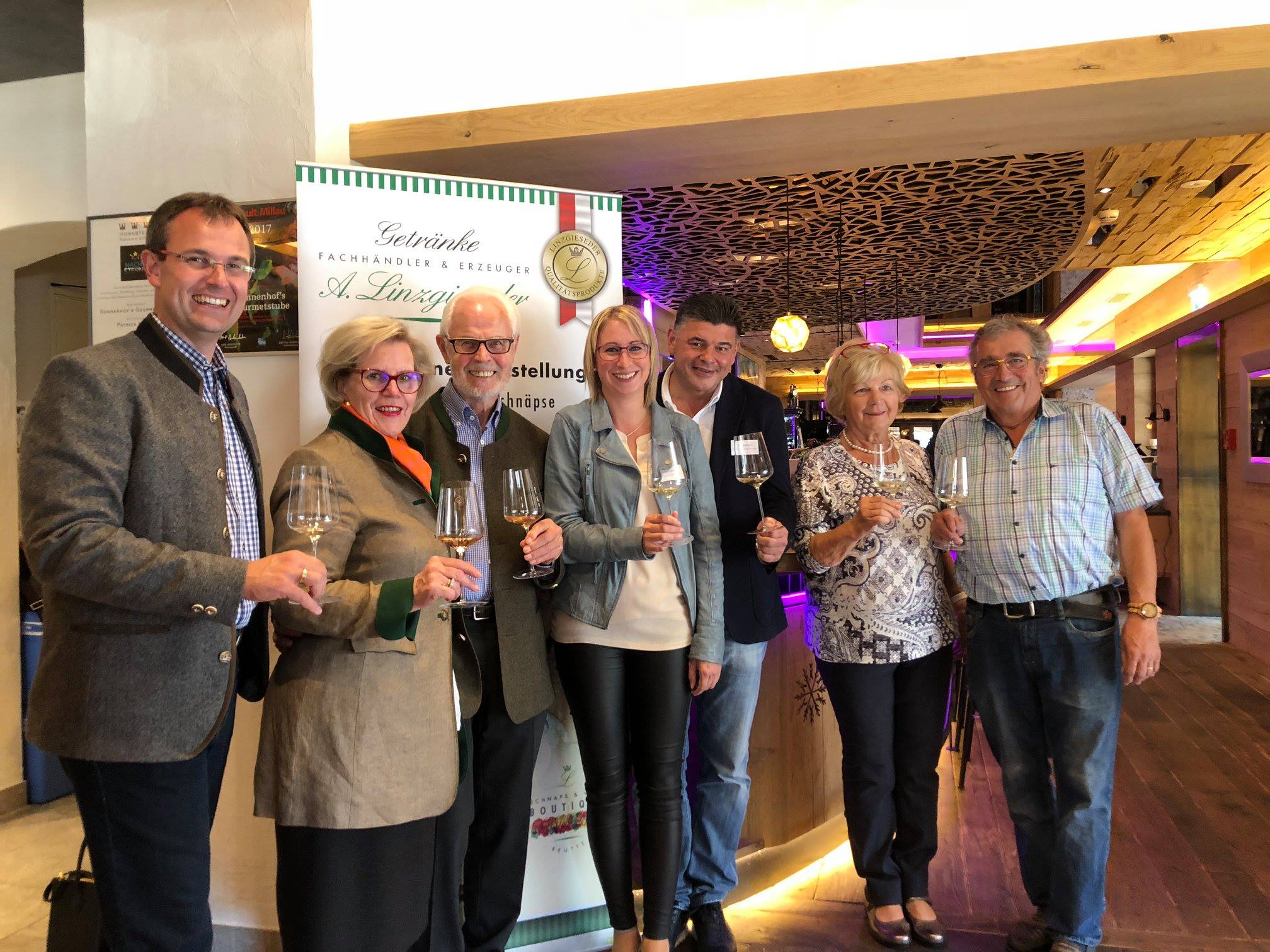 Von links nach rechts sind auf dem Bild Alfred Linzgieseder, seine Mutter, sein Vater Arnold, die Sommelier-Dame Angelika mit ihrem Partner sowie ortsansässige Gastronomen zu sehen. Alle halten ein Weinglas in der Hand und präsentieren es dem Fotografen. 